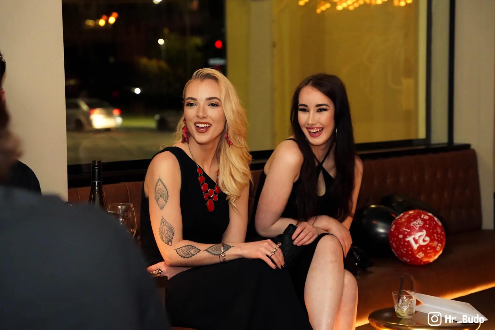 Two women in black dresses seated and smiling at a candid birthday party in Canberra