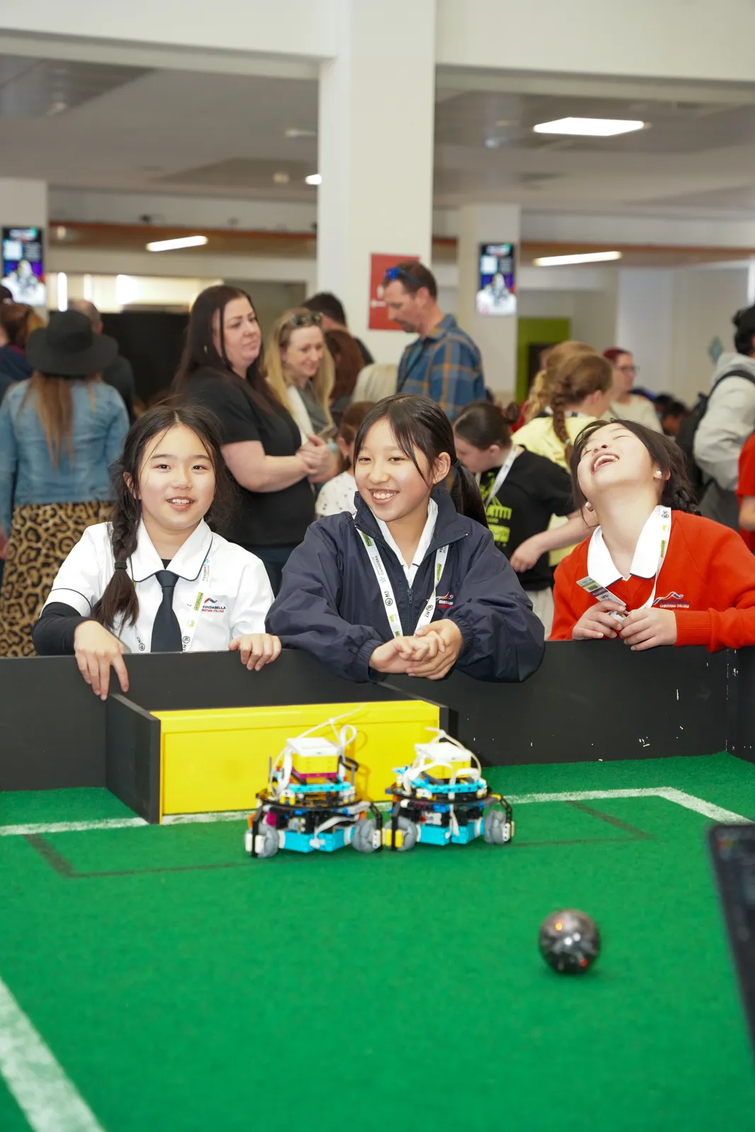 Smiling school students watching small robots on a green field at a Canberra school event