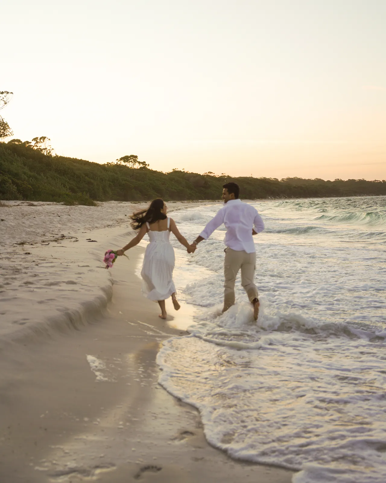 Couple holding hands and running through the shallows on a beach at sunset