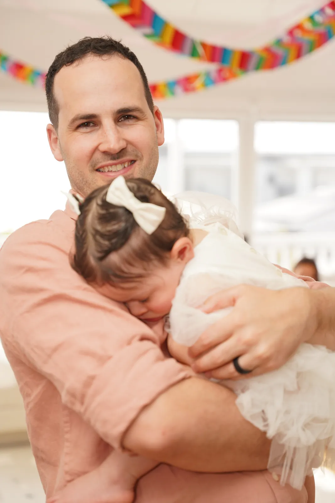 Father cuddling his toddler daughter in a bow at a first birthday party in Canberra