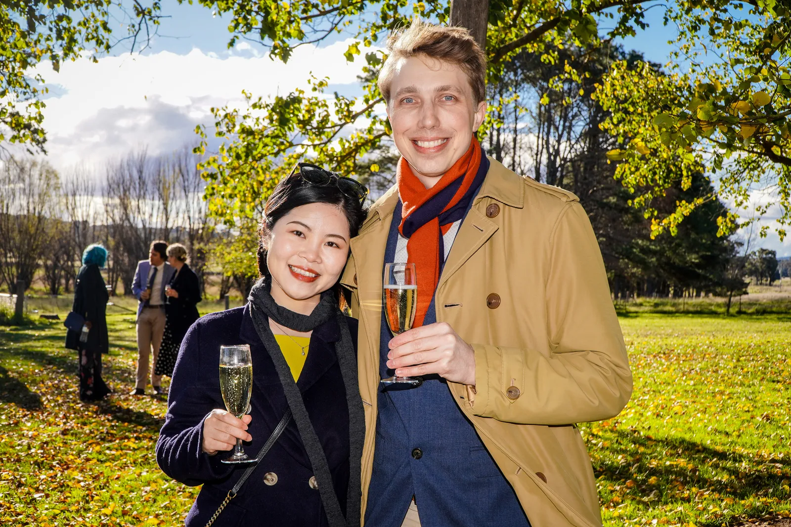 Two friends holding champagne glasses in an autumn park at an outdoor event